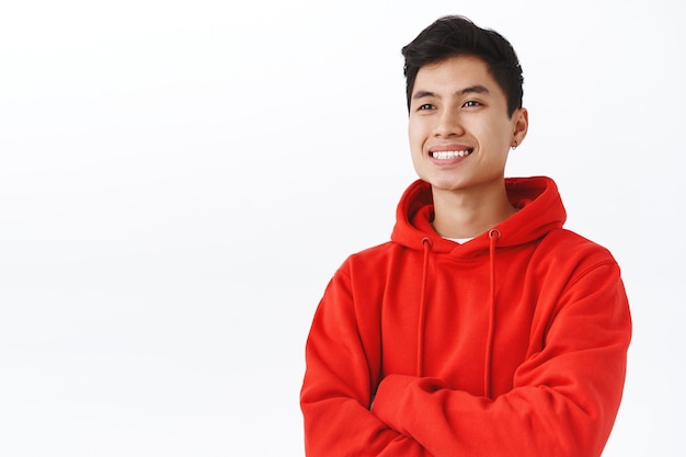 Waist-up portrait of professional, successful young asian man seeing good profit, made investment or finished deal, looking pleased, gaze away satisfied with beaming smile, white wall.