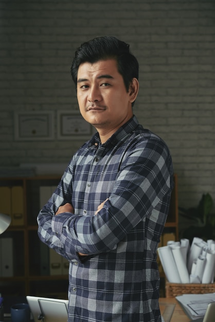 Waist up shot of Asian man standing arms folded in an architect office