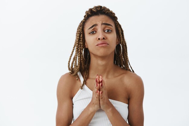 Waist-up shot of beautiful stylish and attractive african american woman with dreadlocks in top holding hands in pray