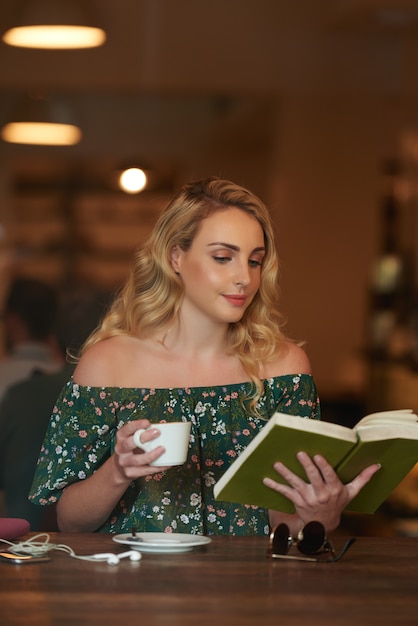 Waist up shot of carefree woman reading a book in a coffee shop