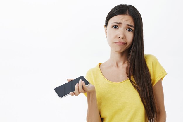 Waist-up shot of displeased moody and unimpressed attractive stylish woman being fed up with old model of smartphone