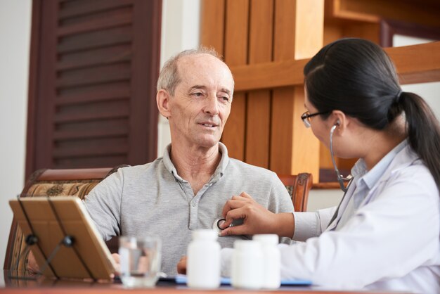 Waist up shot of female doctor listening to heartbeat of senior man