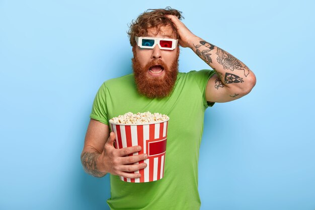 Waist up shot of frightened ginger man keeps hand on head, looks with panic and fear