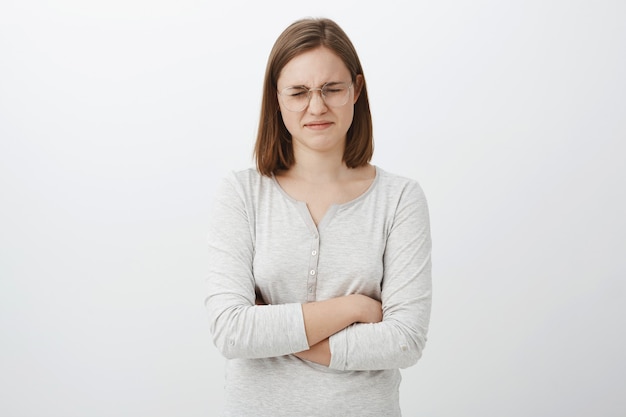 Free photo waist-up shot of gloomy whining girl with short haircut complaining closing eyes and pursing lips crossing hands on chest feeling upset, envy or jealous losing in competition over gray wall