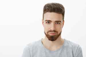 Free photo waist-up shot of handsome sensual and confident young man with beard, moustache and blue eyes smiling looking sincere and self-assured as with delighted smile against gray wall