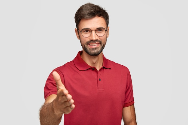 Waist up shot of happy unshaven man gives handshake, greets with someone, smiles sincerely