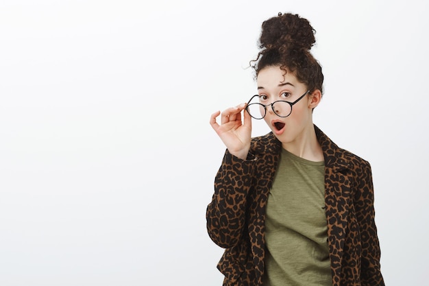 Waist-up shot of impressed surprised curly-haired attractive female in leopard coat, taking off glasses and dropping jaw from impressive amazing rumor