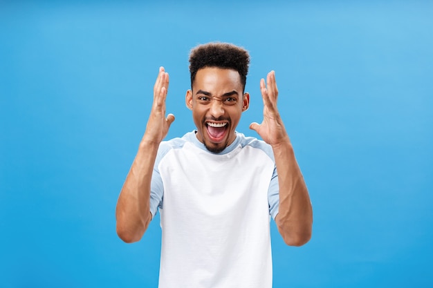 Waist-up shot of man going furious being in rage shouting and yelling from anger stressing out and arguing with girlfriend having fight shaking raised arms standing over blue background. Copy space