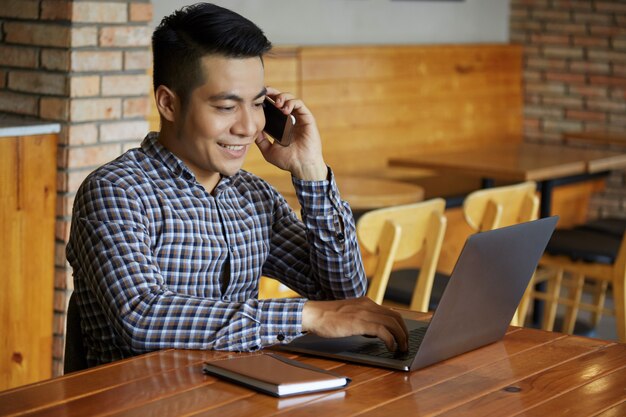 Waist up shot of man working at the laptop while talking on the phone