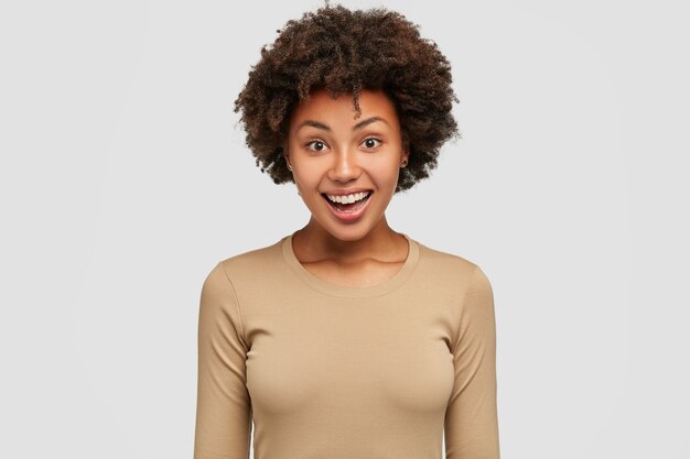 Waist up shot of pleased happy Afro woman rejoices success at work