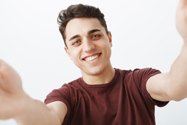 Waist-up shot of pleased happy young european man in trendy red t-shirt