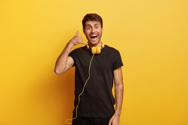 Waist up shot of positive Caucasian man makes call gesture