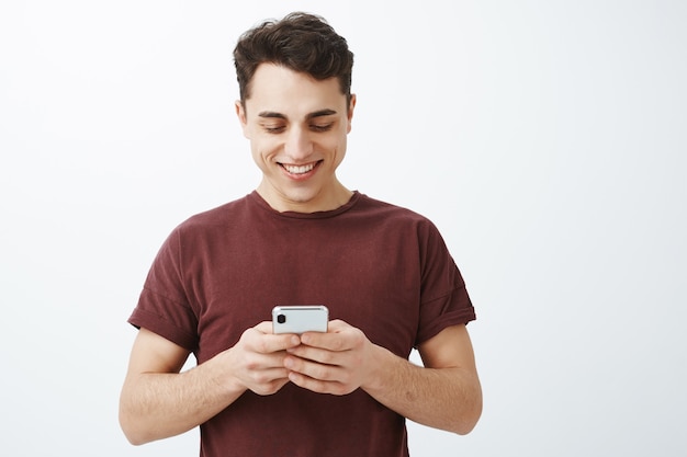 Waist-up shot of positive friendly handsome man in red t-shirt with smartphone