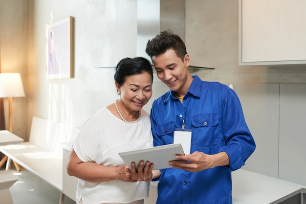 Waist up shot of repairman showing a digital questionnaire to the senior client