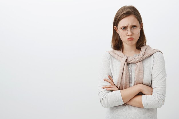 Waist-up shot of sad unhappy and gloomy cute girl with flapped ear frowning and sulking crossing arms over body feeling jealous or regret being punished by parents standing upset over gray wall