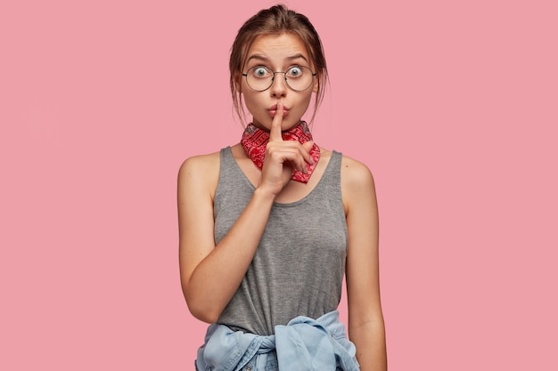 Free photo waist up shot of surprised caucasian woman shocked with unexpected rumours, shows hush gesture