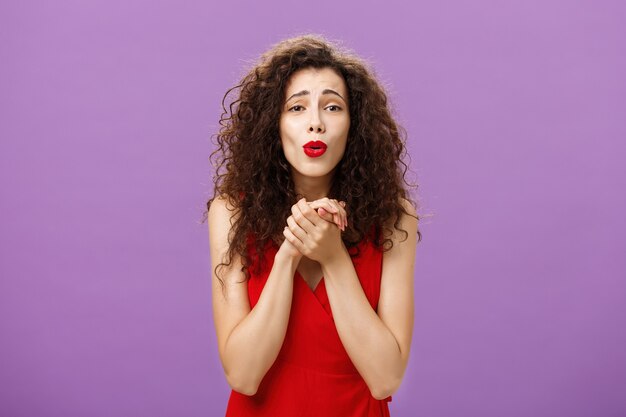 Waist-up shot of woman gazing at heartwarming scene being touched and delighted holding palms togehter over chest folding lips enjoying watching cute puppy posing pleased over purple background.