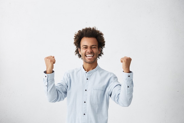 Foto gratuita girovita girato in studio di fortunato riuscito studente di razza mista con taglio di capelli afro che esclama