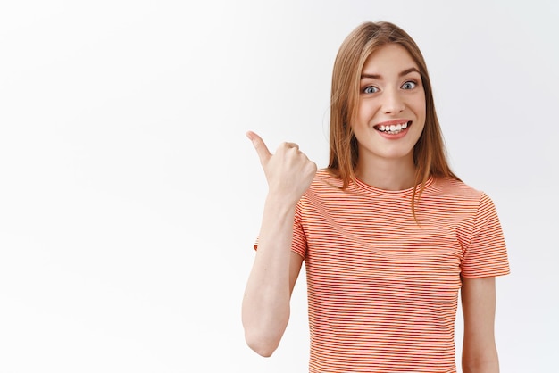 Free photo waistup attractive cheerful young caucasian woman in striped tshirt smiling amused and enthusiastic pointing left with thumb invite take look interesting promo standing white background