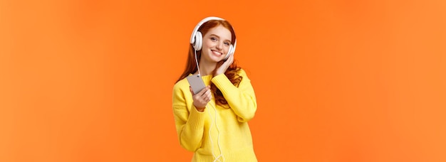Бесплатное фото waistup портрет веселая милая молодая женщина с рыжими волосами слушает музыку в наушниках наклоняет голову и