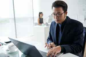 Free photo waistup shot of asian businessman working at laptop in coworking space