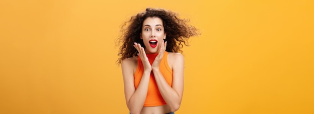 Free photo waistup shot of charmed enthusiastic attractive female with curly hairstyle in cropped top holding p