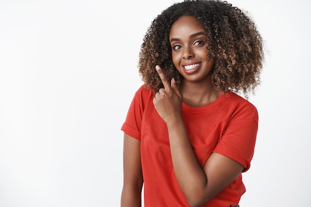 Waistup shot of charming friendlylooking african american woman suggesting cool promotion pointing at upper left corner and smiling