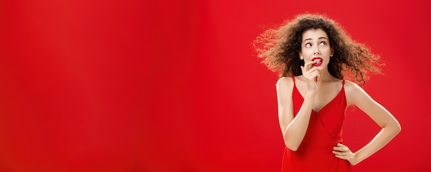 Foto gratuita immagine di vita di una donna insicura e preoccupata con i capelli ricci in abito da sera rosso