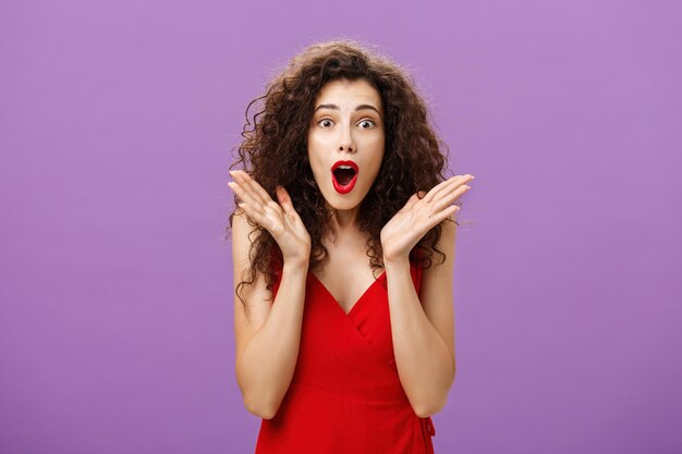 Waistup shot of excited and amazed expressive elegant adult curlyhaired woman with red lipstick in e...