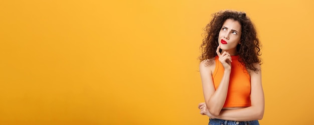 Free photo waistup shot of perplexed thoughtful and smart female with curly hairstyle in red lipstick and cropp