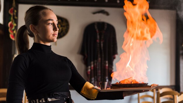 Waiter carrying dish with meat on fire