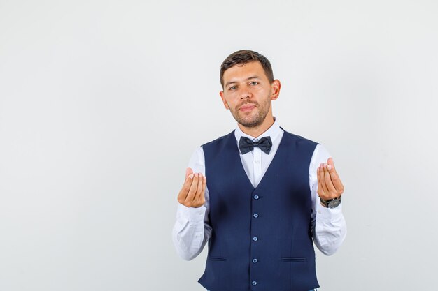 Waiter doing italian gesture and smiling in shirt, vest, bow tie front view.