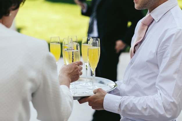 Waiter dressed in white carries glasses with champagne