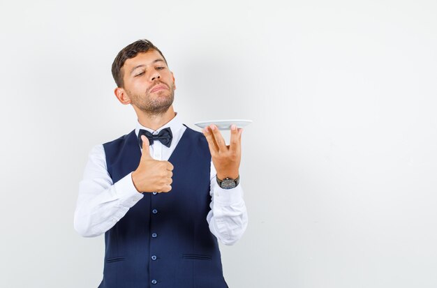 Waiter holding empty plate with thumb up in shirt, vest front view.