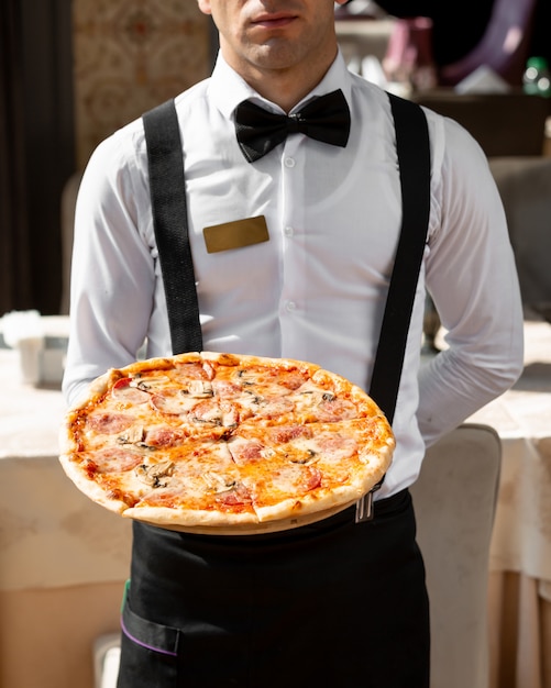 Waiter holding pepperoni pizza with mushrooms