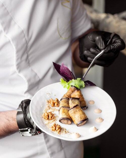 Waiter holding a plate of fried aubergine wraps with walnuts