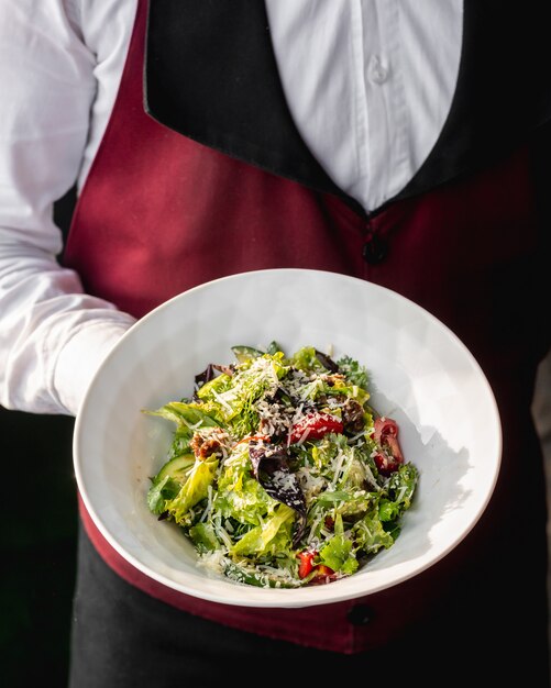 Waiter holding a plate of green salad with dried tomato