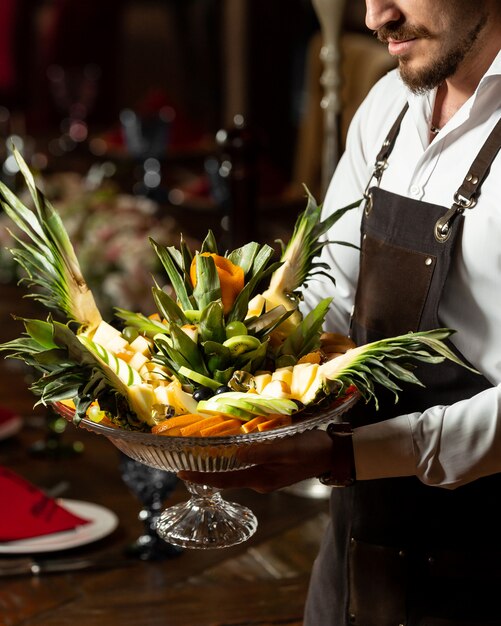 Free photo waiter holding a platter of fruit mix with original serving