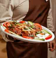 Free photo waiter holding a platter of iskender kebab served with yoghurt and vegetable slices