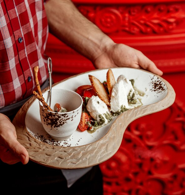 Waiter holding a platter of tomato and cheese salad with pesto sauce