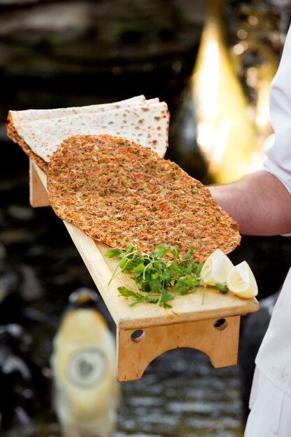 Waiter holding wooden stand with turkish pizza lahmajun with lemon and parsley