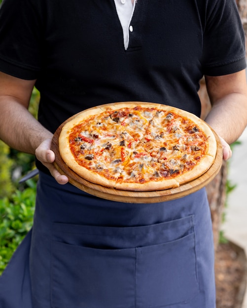 Waiter holds meat pizza with red and yellow bell pepper