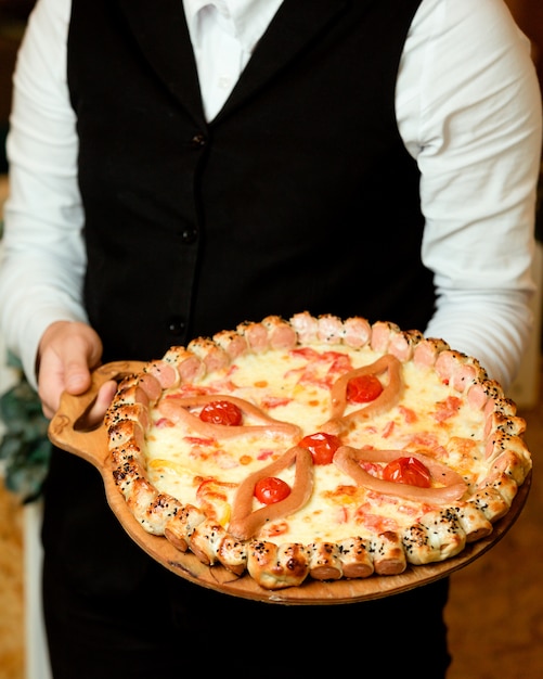 웨이터는 토마토 치즈와 소시지 조각으로 소시지 피자를 보유하고 있습니다.