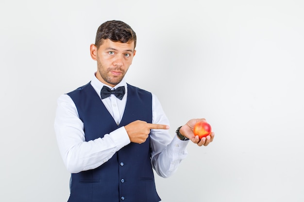 Waiter pointing finger at nectarine in shirt, vest and looking serious , front view.