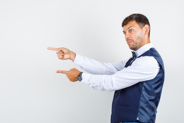 Waiter pointing fingers to side in shirt, vest and looking motivated. .