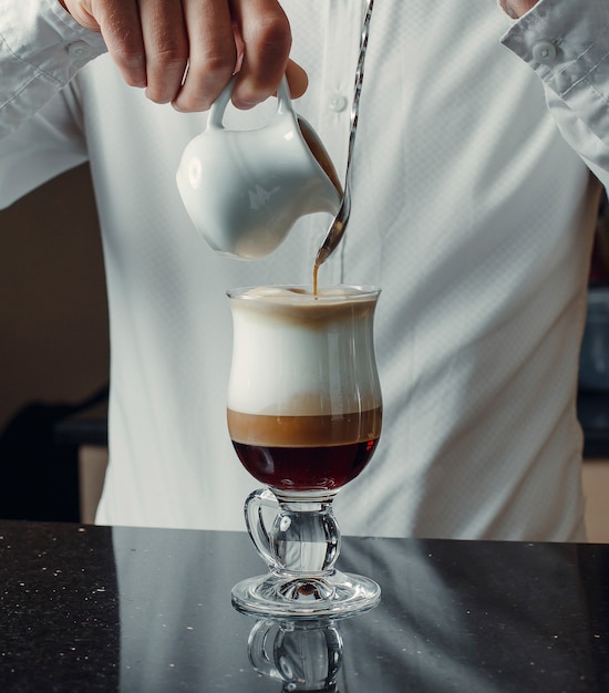 Waiter pouring caramel into triple-color coffee drink from milk pot