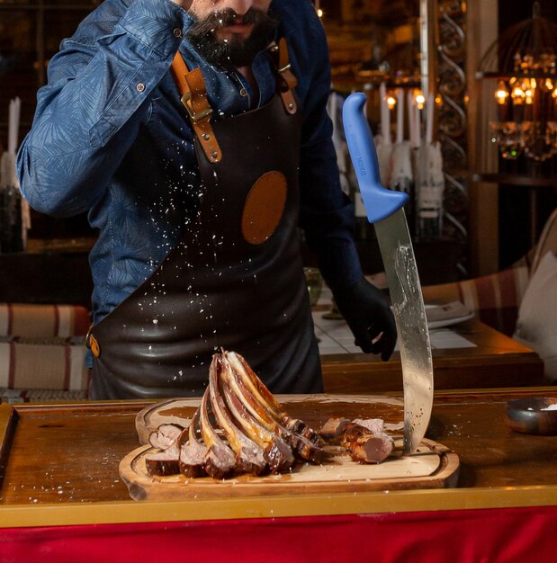 Waiter pouring salt over lamb rib kebab served on wooden board