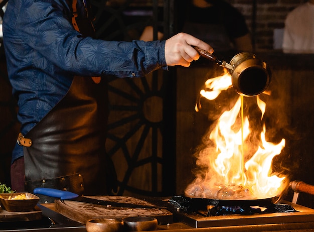 ウェイターはフライパンで燃えているステーキに油を注ぐ