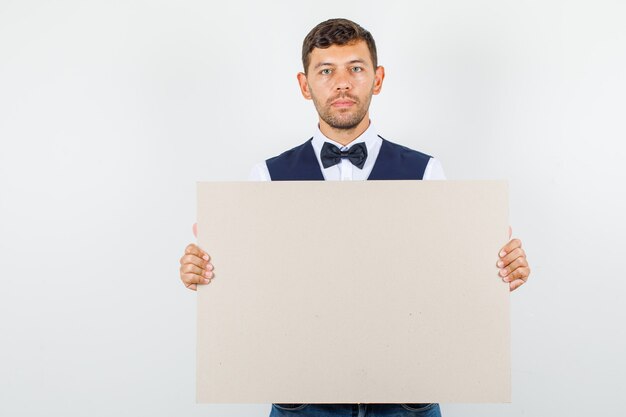 Waiter in shirt, vest holding blank canvas and looking serious , front view.