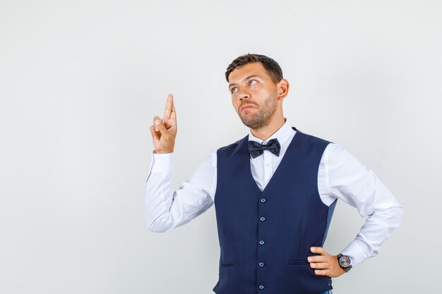 Waiter in shirt, vest, looking up with crossed fingers and looking hopeful , front view.